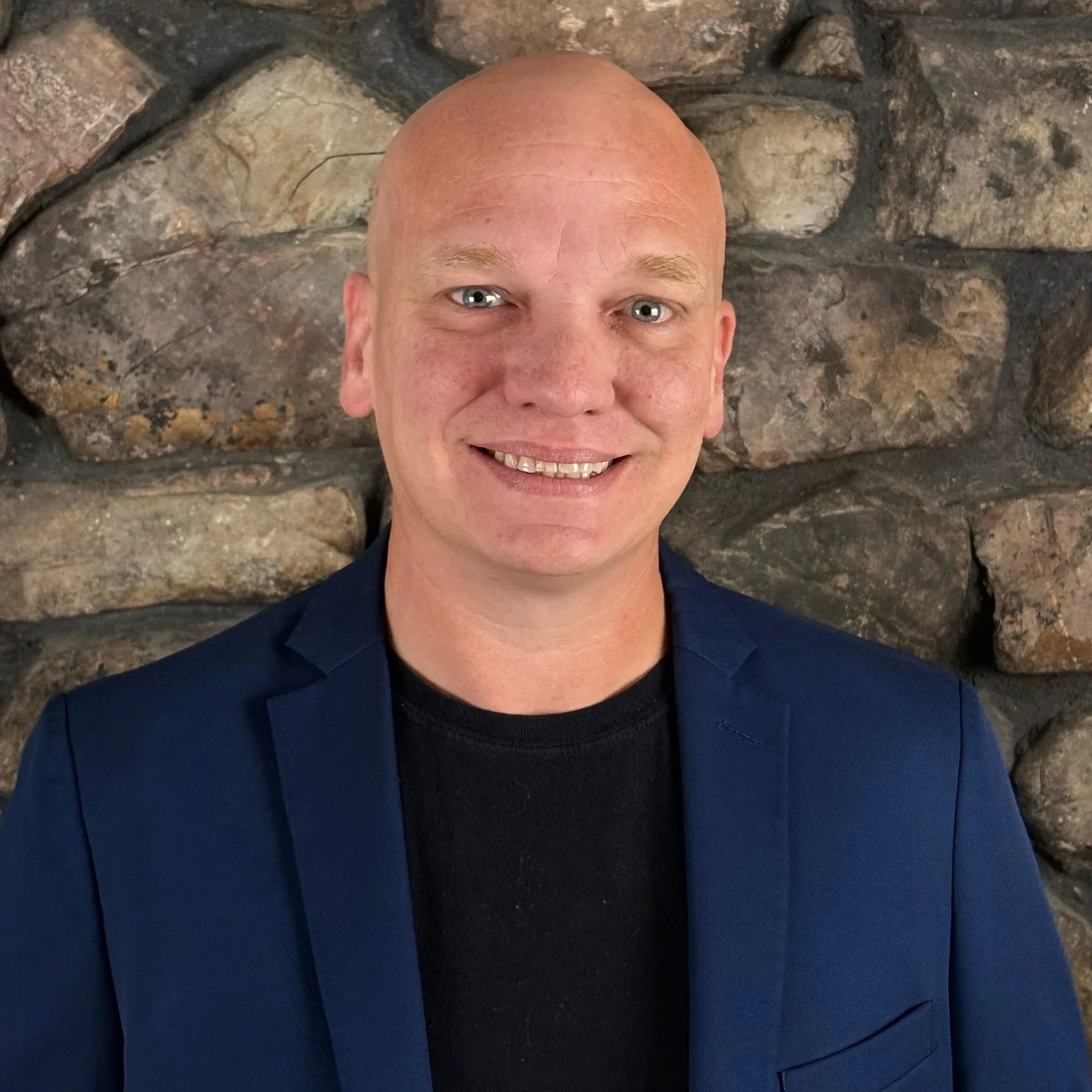 David Carr smiling in a navy jacket against a stone wall